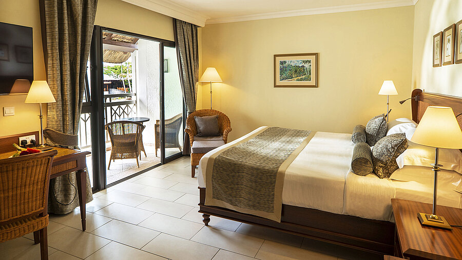 Bright hotel room with balcony, cozy reading nook, desk, and modern furniture