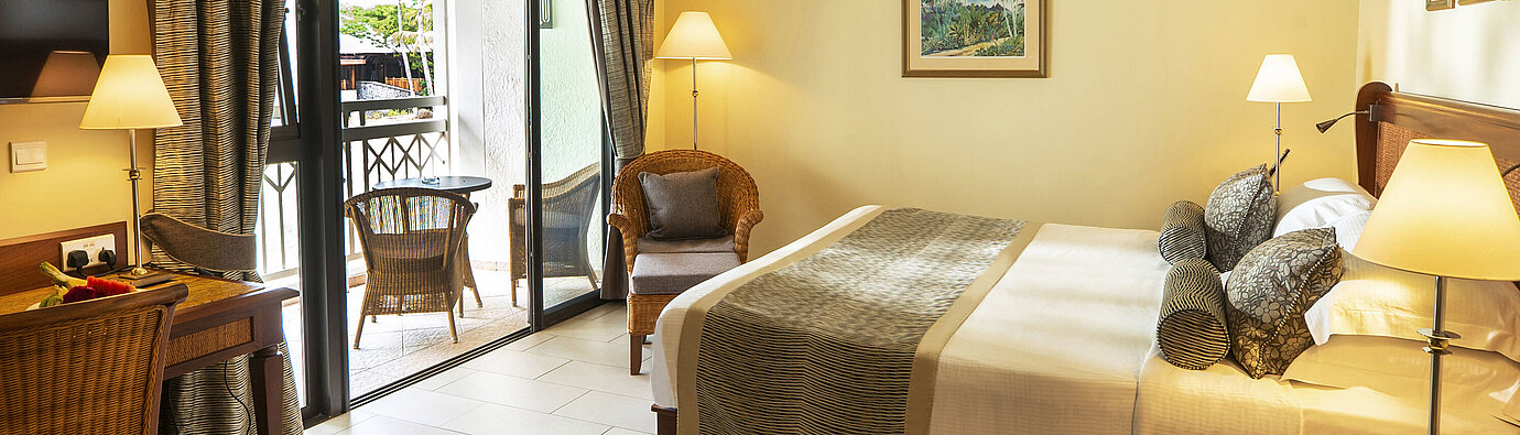 Bright hotel room with balcony, cozy reading nook, desk, and modern furniture