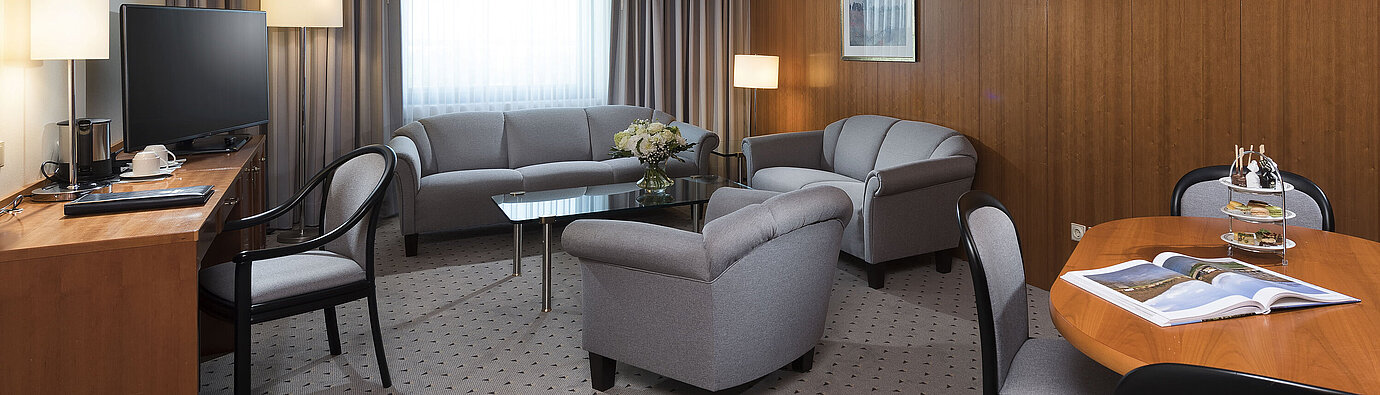 Junior Suite with elegant living area, sofa, armchairs, desk, and TV at Maritim Hotel Hannover.