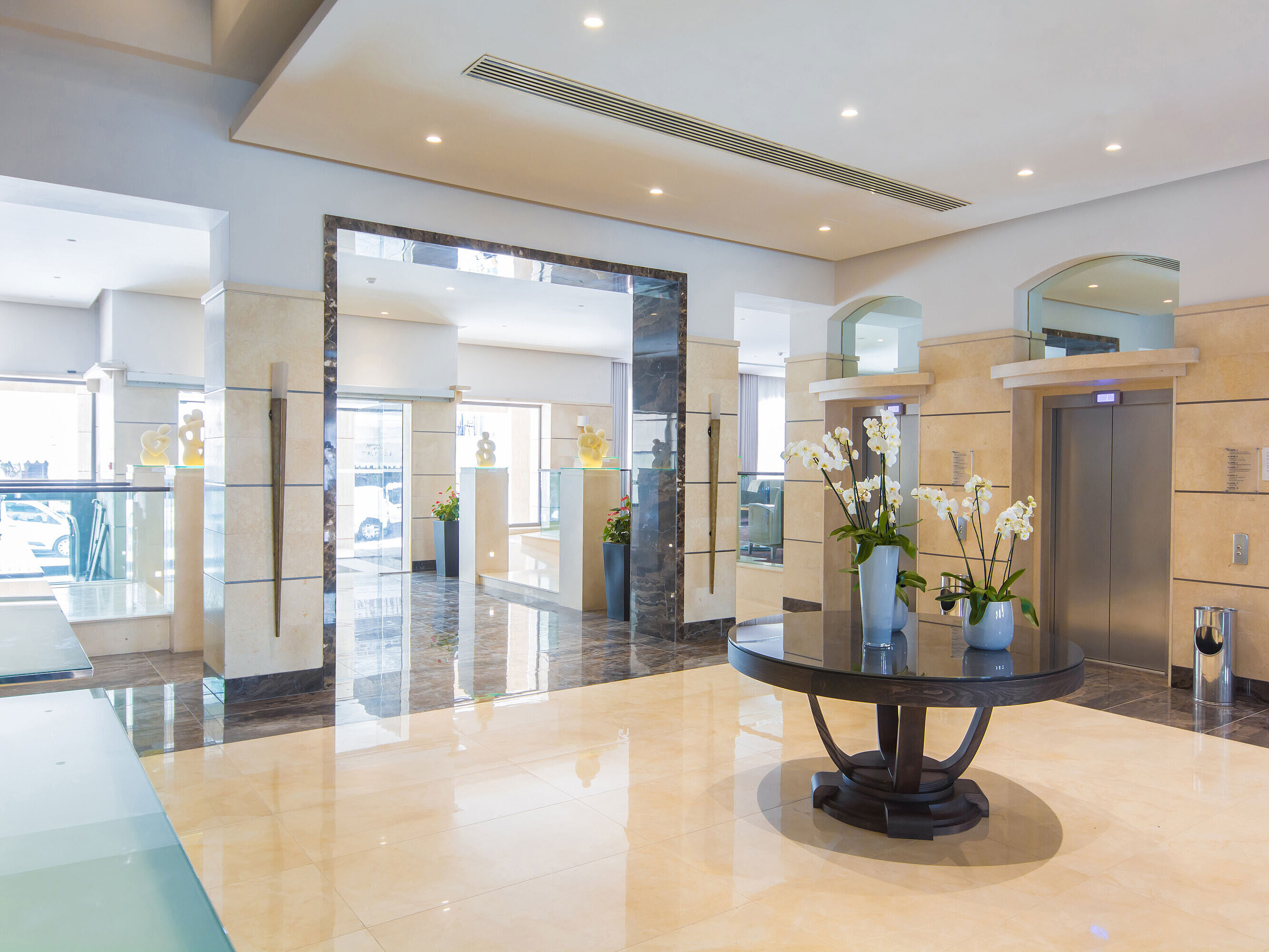 Bright hotel lobby with lifts, marble floor, sculptures and stylish ambience