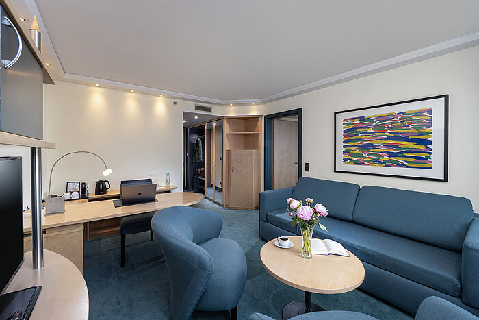 Family suite with desk, sofa, armchairs and flowers at Maritim proArte Hotel Berlin