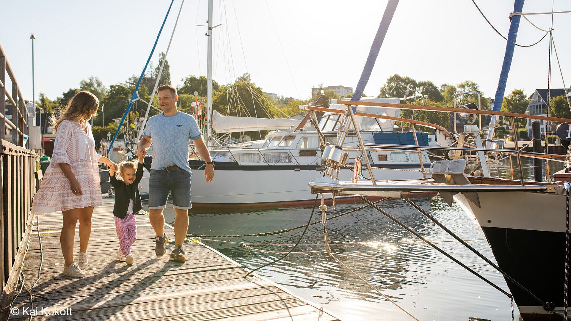 Family walking across harbour bridge with sailing boats in background on sunny day