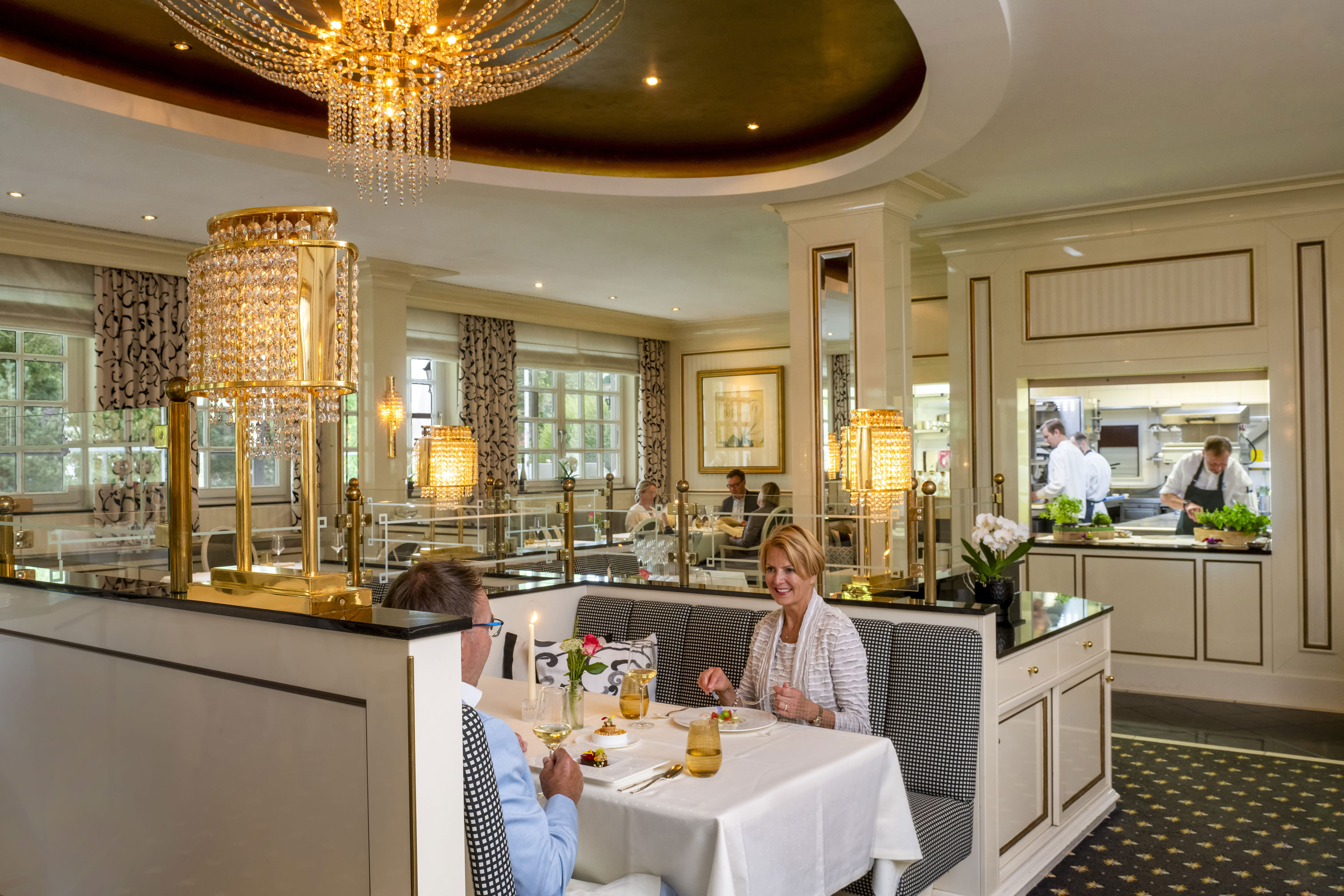 Couple enjoying a fine dinner at the luxurious Orangerie restaurant in Maritim Timmendorfer Strand with a view of the kitchen